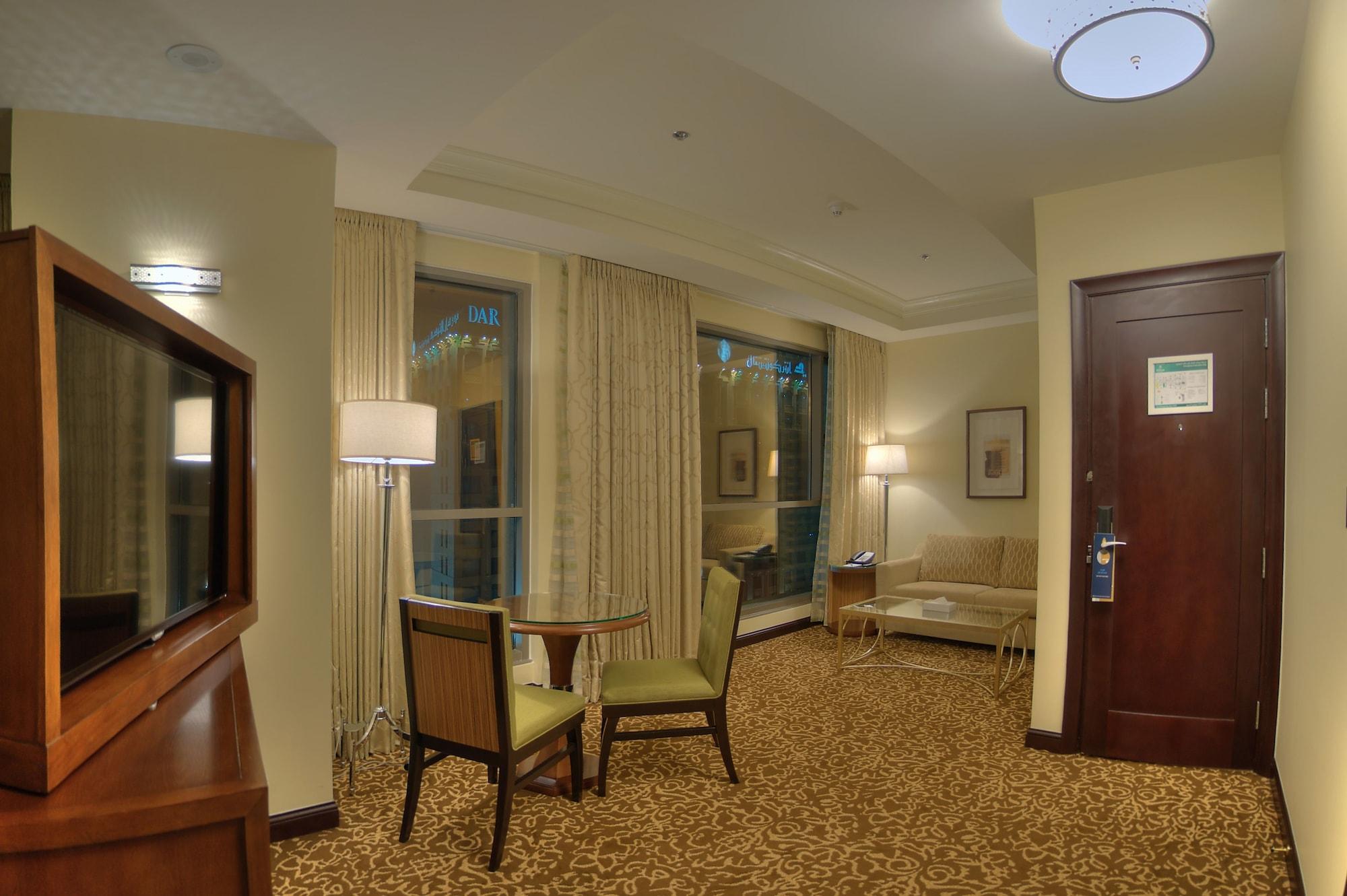 Hilton Suites Jabal Omar Makkah Meca Exterior foto The photo shows a cozy hotel room or suite that features a small seating area. There is a table with two chairs, suggesting a space for dining or working. A comfortable-looking sofa is positioned against the wall, next to a window covered with light-