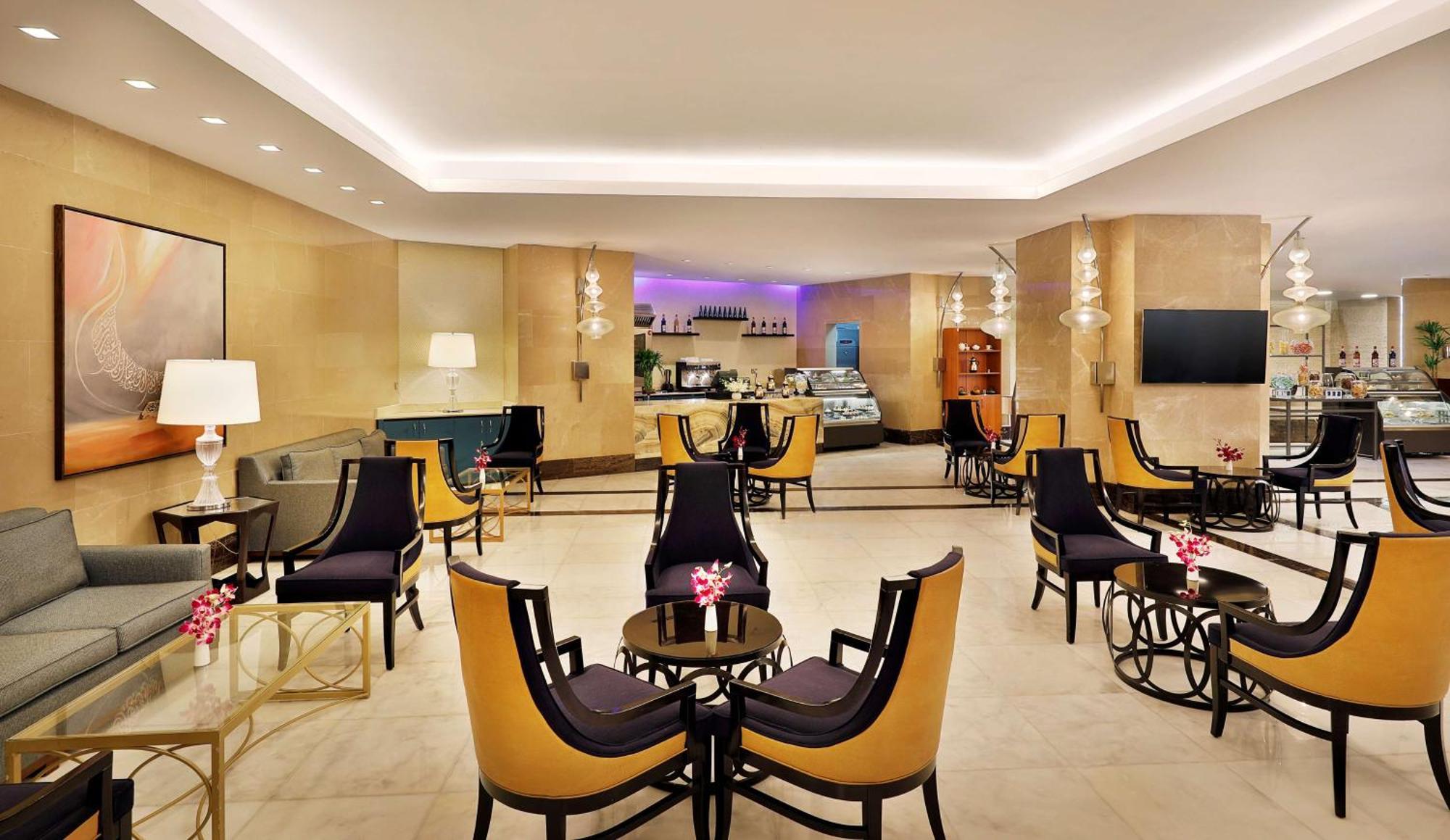 Hilton Suites Jabal Omar Makkah Meca Exterior foto The photo depicts a stylish and contemporary lounge area, featuring elegant furniture arranged in a cozy setting. There are several black and gold accent chairs with small glass tables in front of them, creating small seating groups. The decor includ