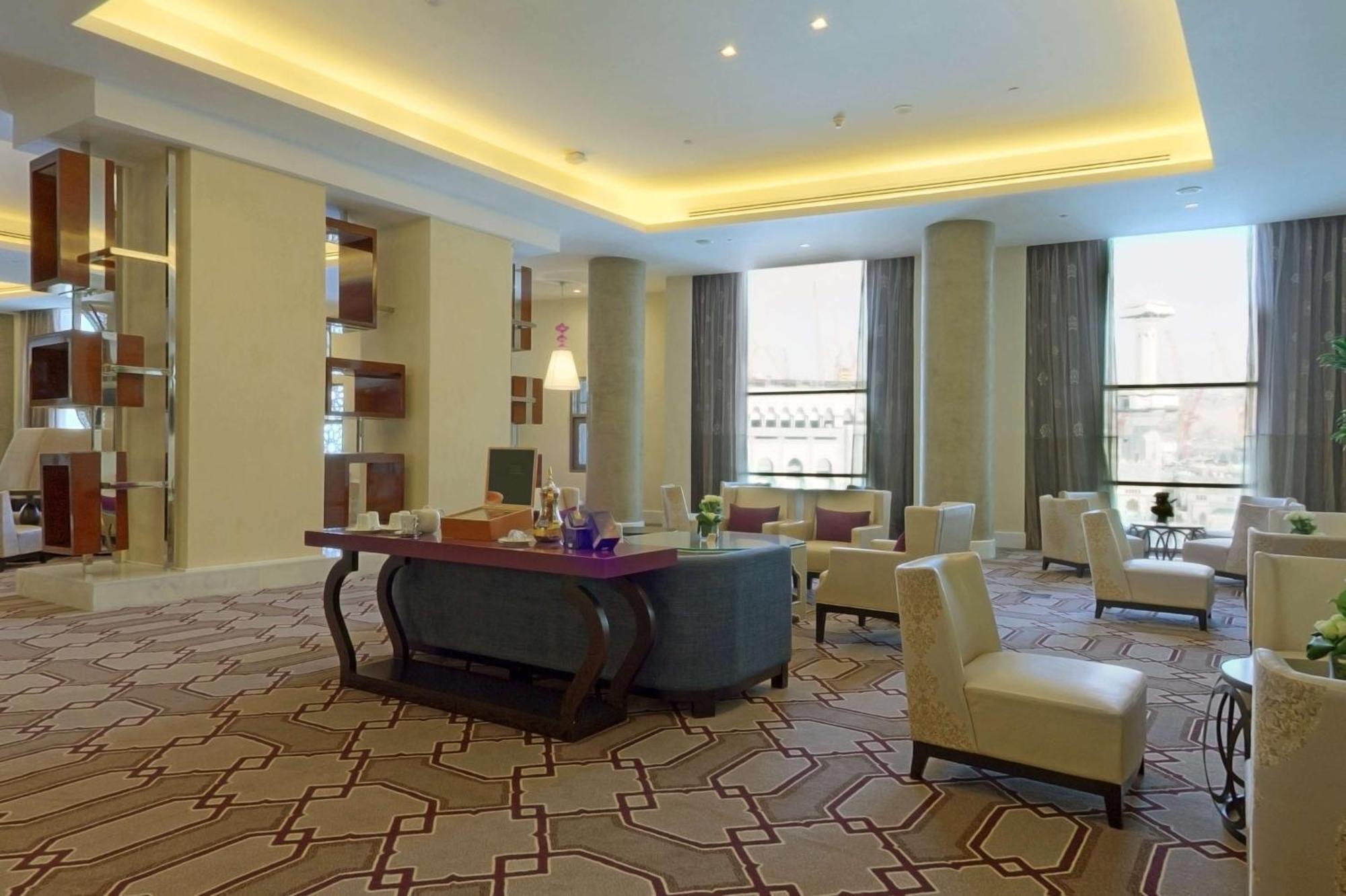 Hilton Suites Jabal Omar Makkah Meca Exterior foto The photo shows a spacious and elegantly designed lounge area. The room features a modern aesthetic with soft lighting emanating from the ceiling. There are several comfortable chairs arranged around a central table, creating a welcoming seating area