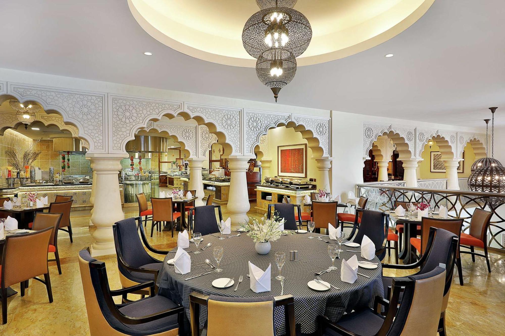 Hilton Suites Jabal Omar Makkah Meca Exterior foto The photo shows an elegantly designed restaurant interior. The space features a round dining table set with plates, glasses, and folded napkins. Surrounding the table are modern, comfortable chairs. The walls are adorned with intricate architectural 
