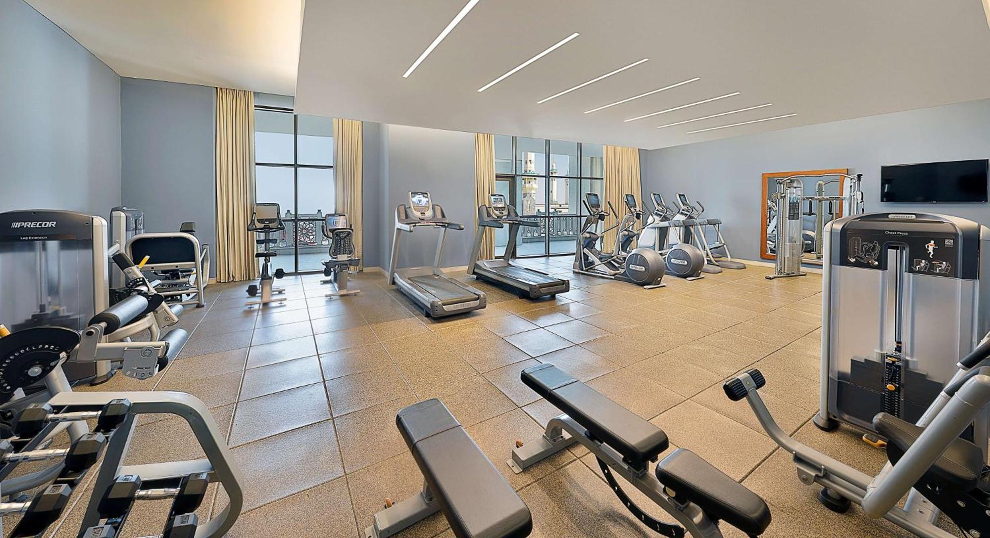 Hilton Suites Jabal Omar Makkah Meca Exterior foto The photo shows a modern gym or fitness room. It features several pieces of exercise equipment, including treadmills, elliptical machines, and weight benches. The space has large windows that allow natural light to fill the room. The walls are painte