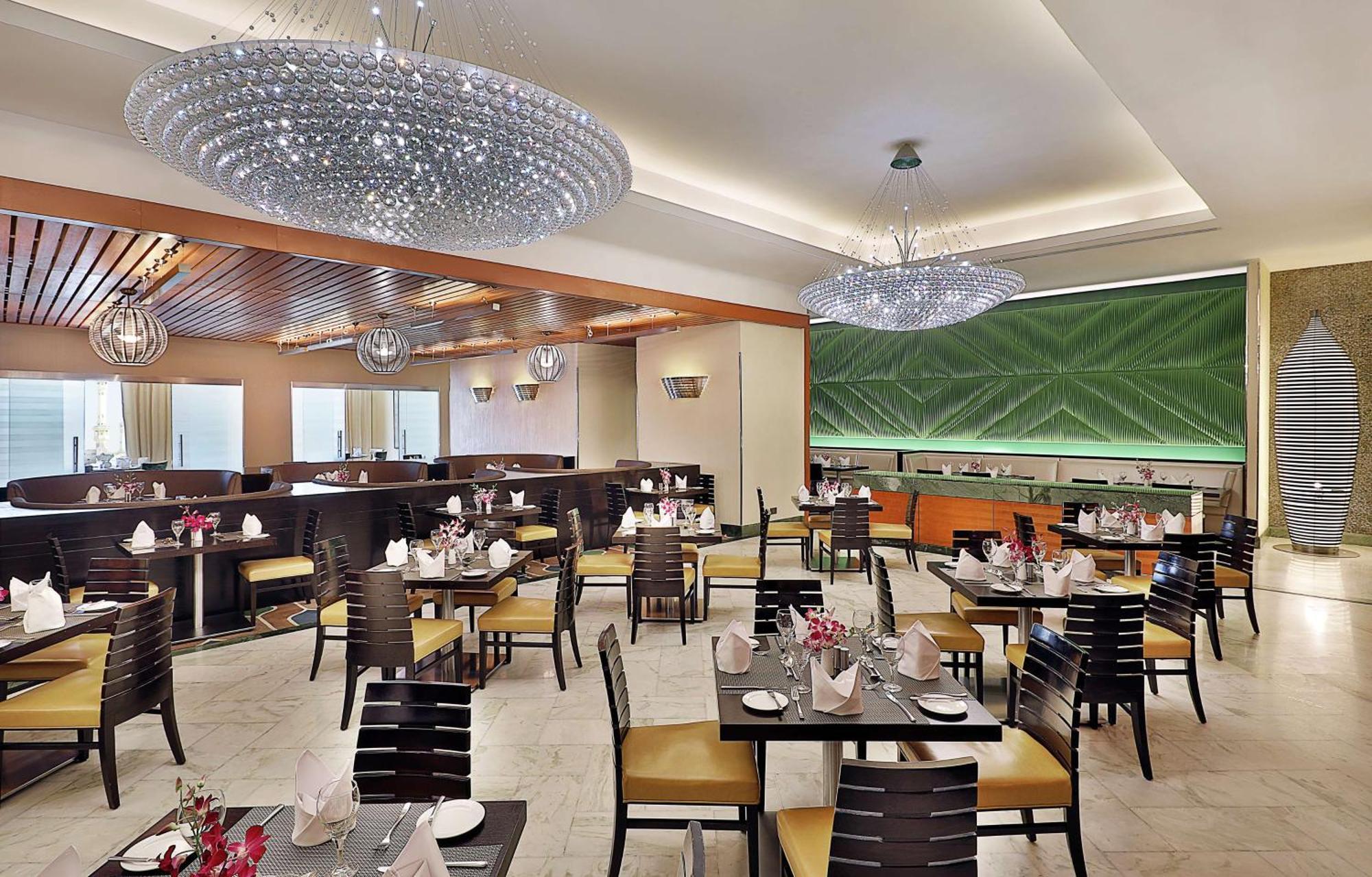 Hilton Suites Jabal Omar Makkah Meca Exterior foto The photo features an elegant restaurant interior. It has a modern design with light-colored walls and wooden accents. The space is furnished with dark wooden tables and chairs, each set with neatly arranged tableware, including napkins and small cen