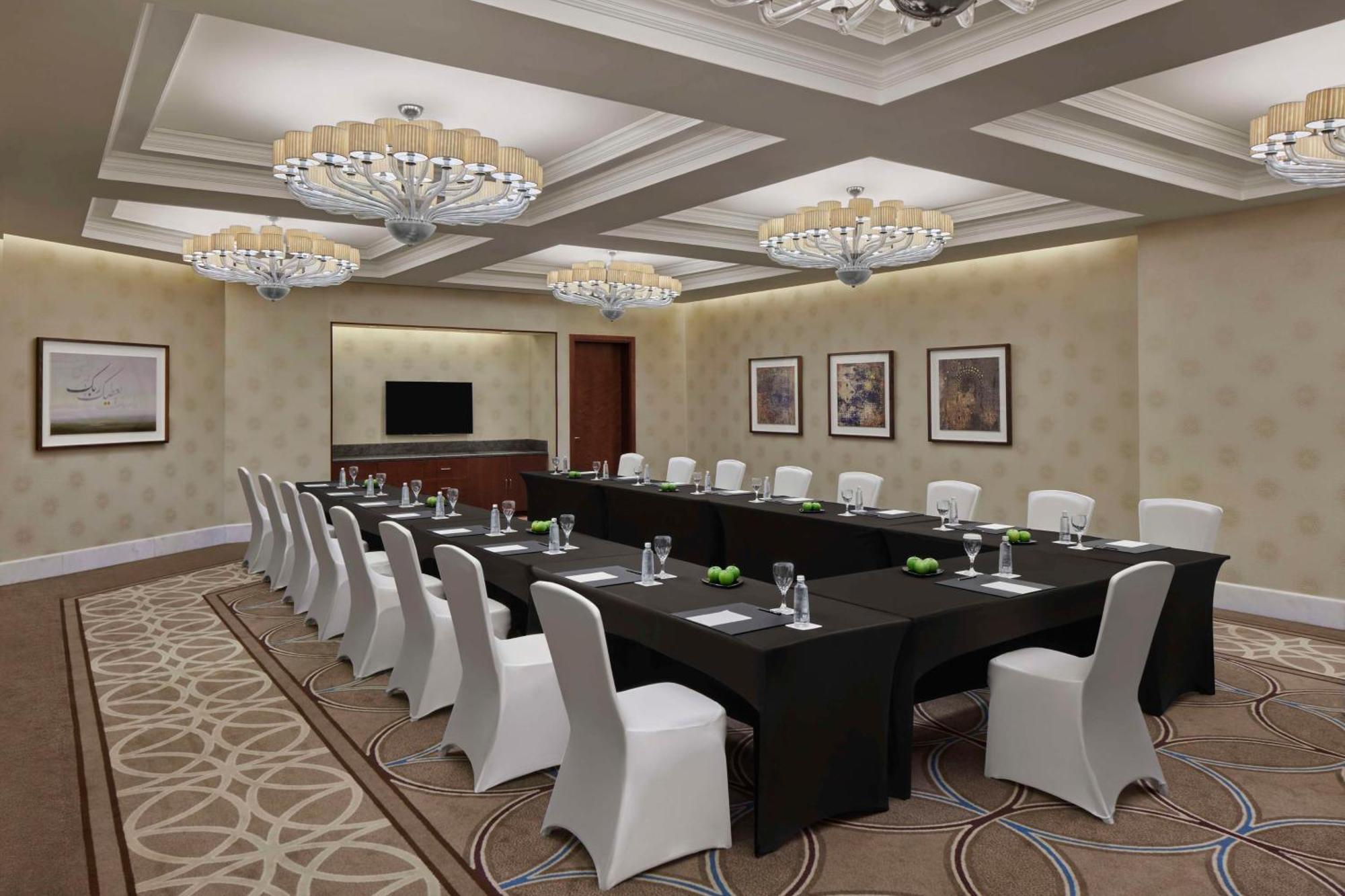 Hilton Suites Jabal Omar Makkah Meca Exterior foto The photo shows a conference room set up for a meeting. There is a long table covered with a black tablecloth, surrounded by white chairs. The room is well-lit with elegant chandeliers hanging from the ceiling. The walls are painted in a light color,