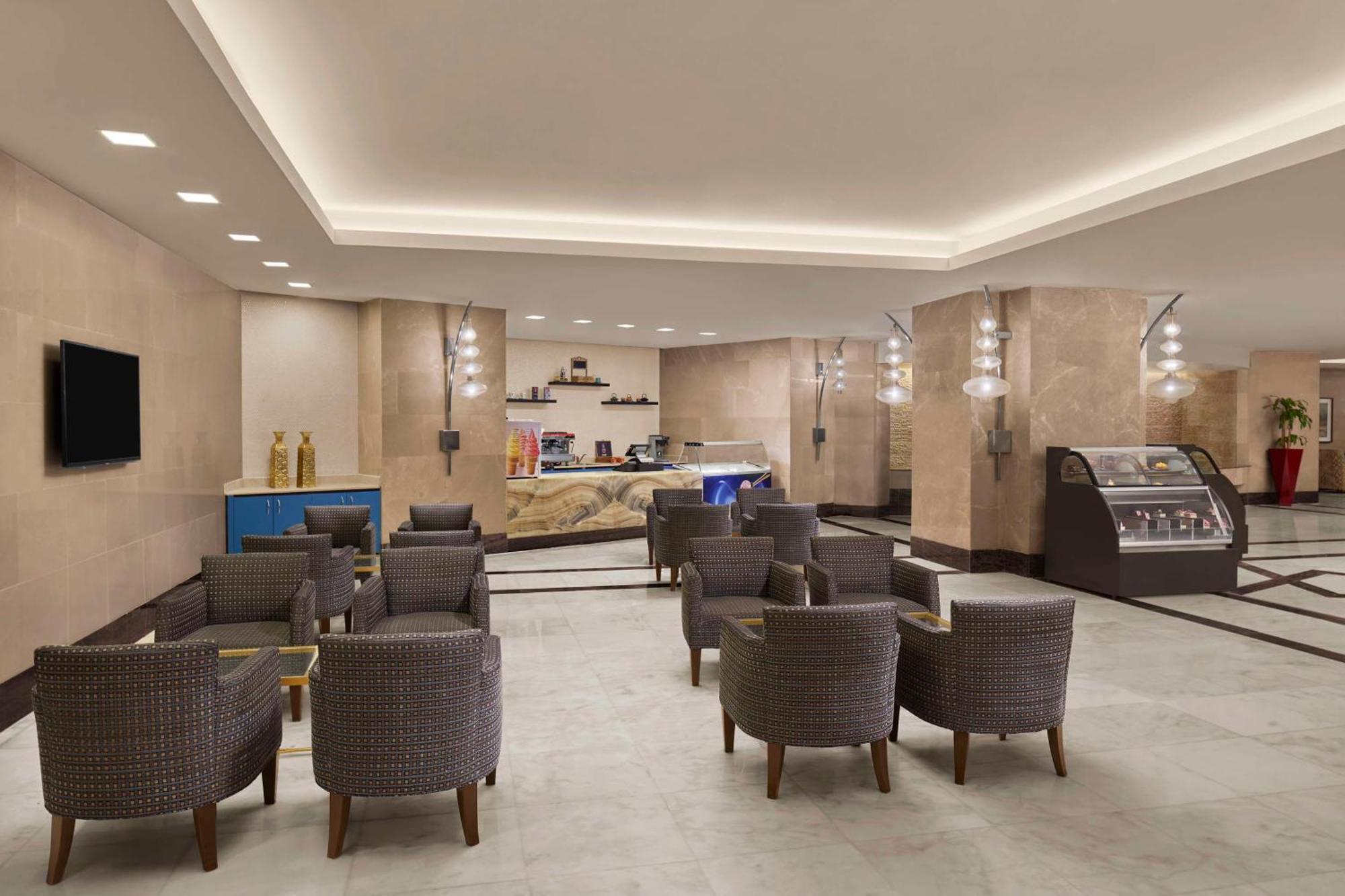 Hilton Suites Jabal Omar Makkah Meca Exterior foto The photo depicts a modern and inviting lobby area, likely in a hotel or similar establishment. The space features a light-colored tiled floor and beige walls, creating a warm ambiance. 

In the foreground, there are several comfortable armchairs arr
