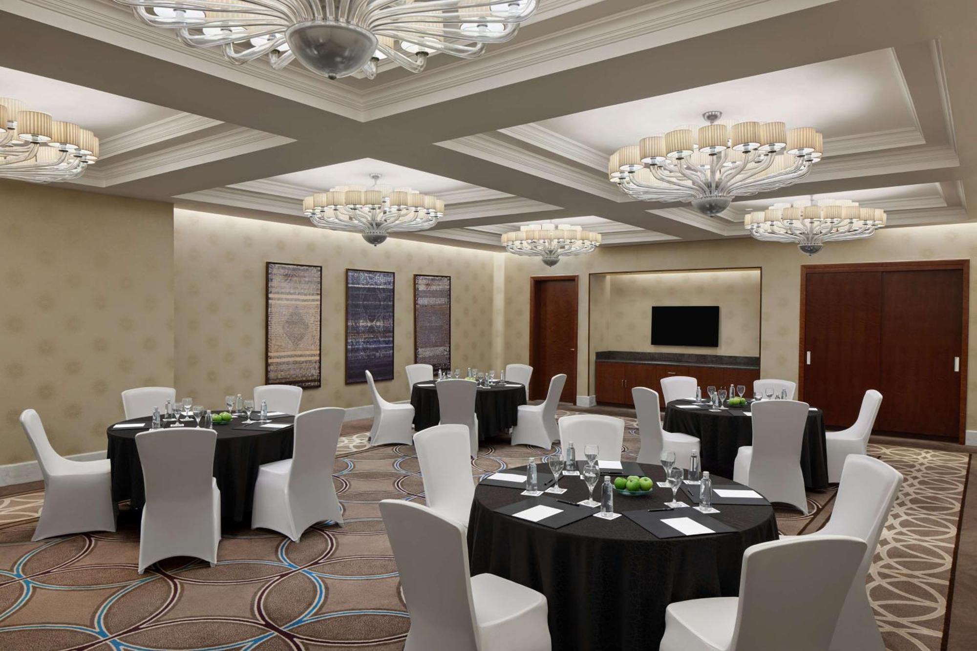 Hilton Suites Jabal Omar Makkah Meca Exterior foto The photo shows an elegant banquet or conference room. It features several round tables covered with black tablecloths, each set with glassware, plates, and small green centerpieces. The chairs are white and neatly arranged around the tables. The roo