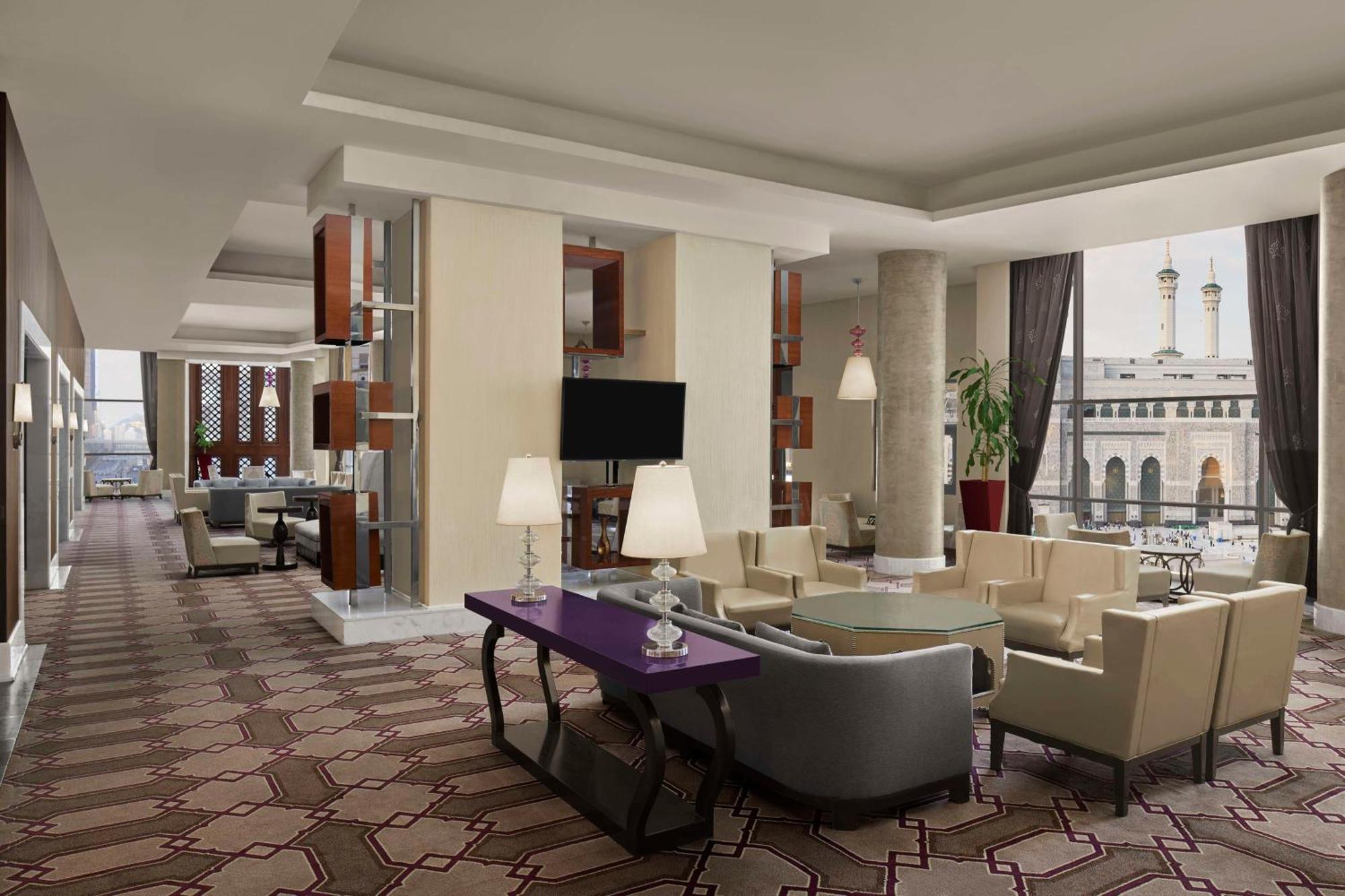 Hilton Suites Jabal Omar Makkah Meca Exterior foto The photo shows a modern lounge area, likely within a hotel or upscale building. The space features elegant, contemporary furniture, including stylish armchairs and sofas arranged around a coffee table. A purple accent table adds a pop of color to th