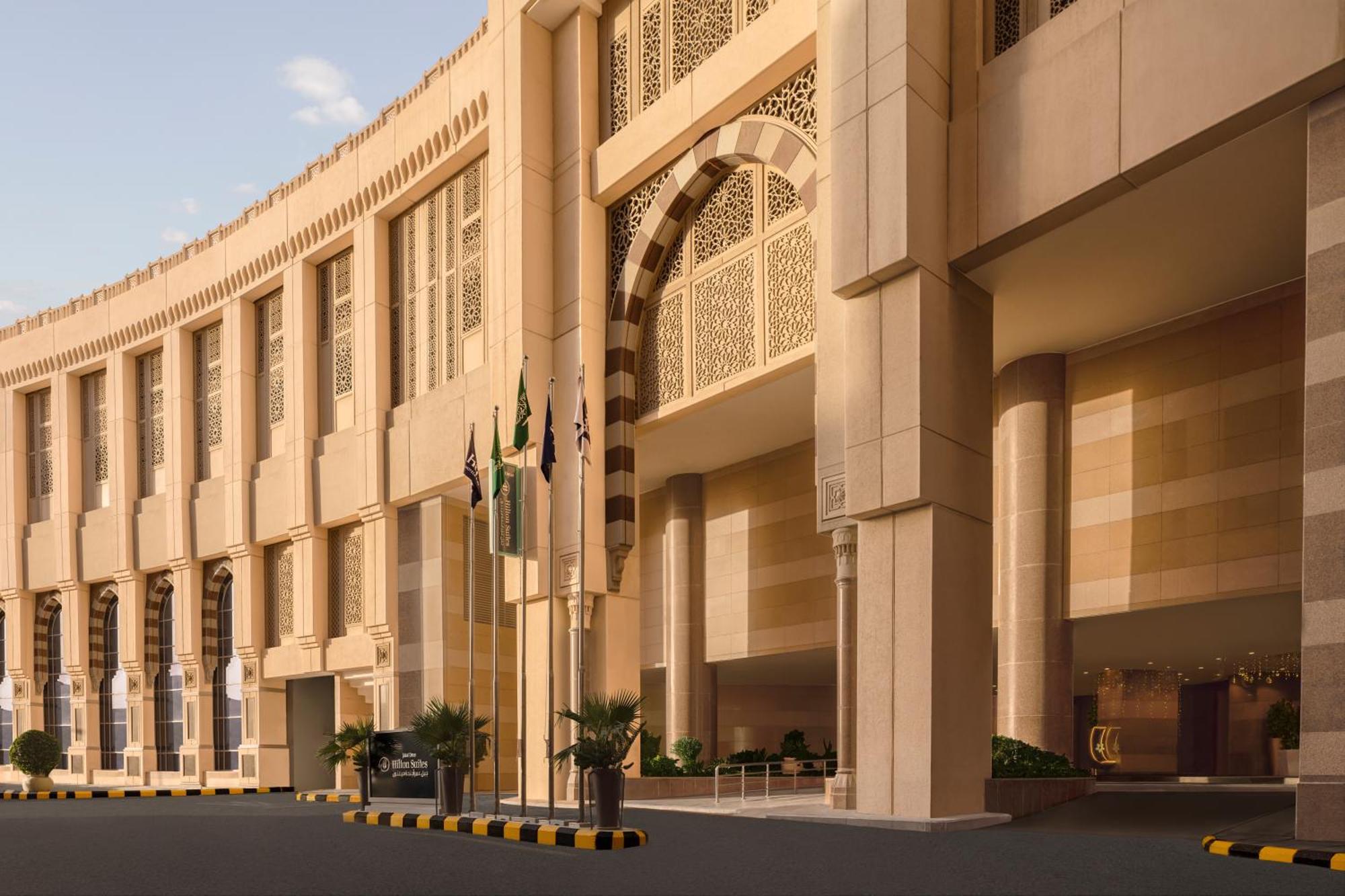 Hilton Suites Jabal Omar Makkah Meca Exterior foto The photo shows a large, modern architectural structure with a grand entrance. The building features a curved facade and intricate design elements, suggesting a blend of contemporary and traditional architectural styles. Several flags are displayed i